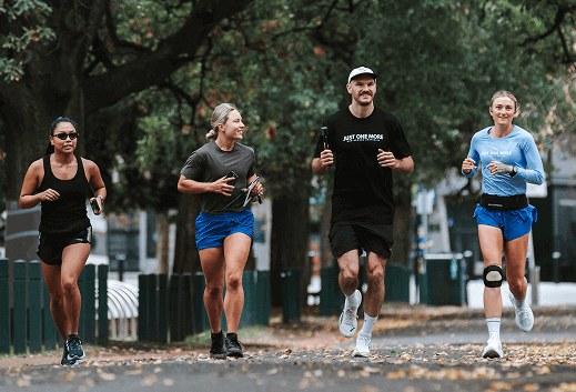 Four adults running together along a tree-lined path