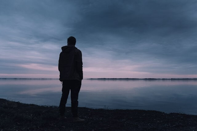 A person standing alone beside calm water under a dark sky