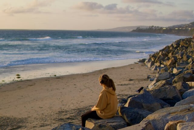 A person sitting alone on rocks beside a beach