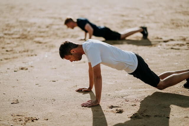 Two men doing push ups at the beach