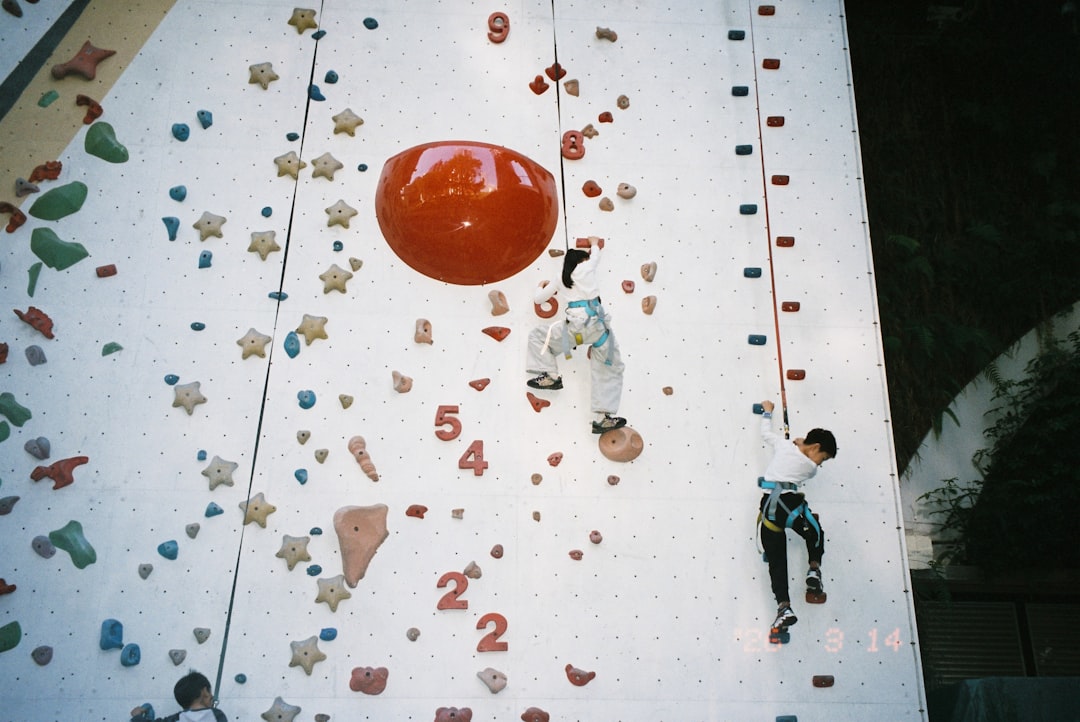 A primary-school-aged child climbing an indoor bouldering wall with a parent watching from below