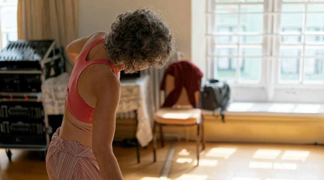 A grey-haired woman stretching sideways in a sunlit room