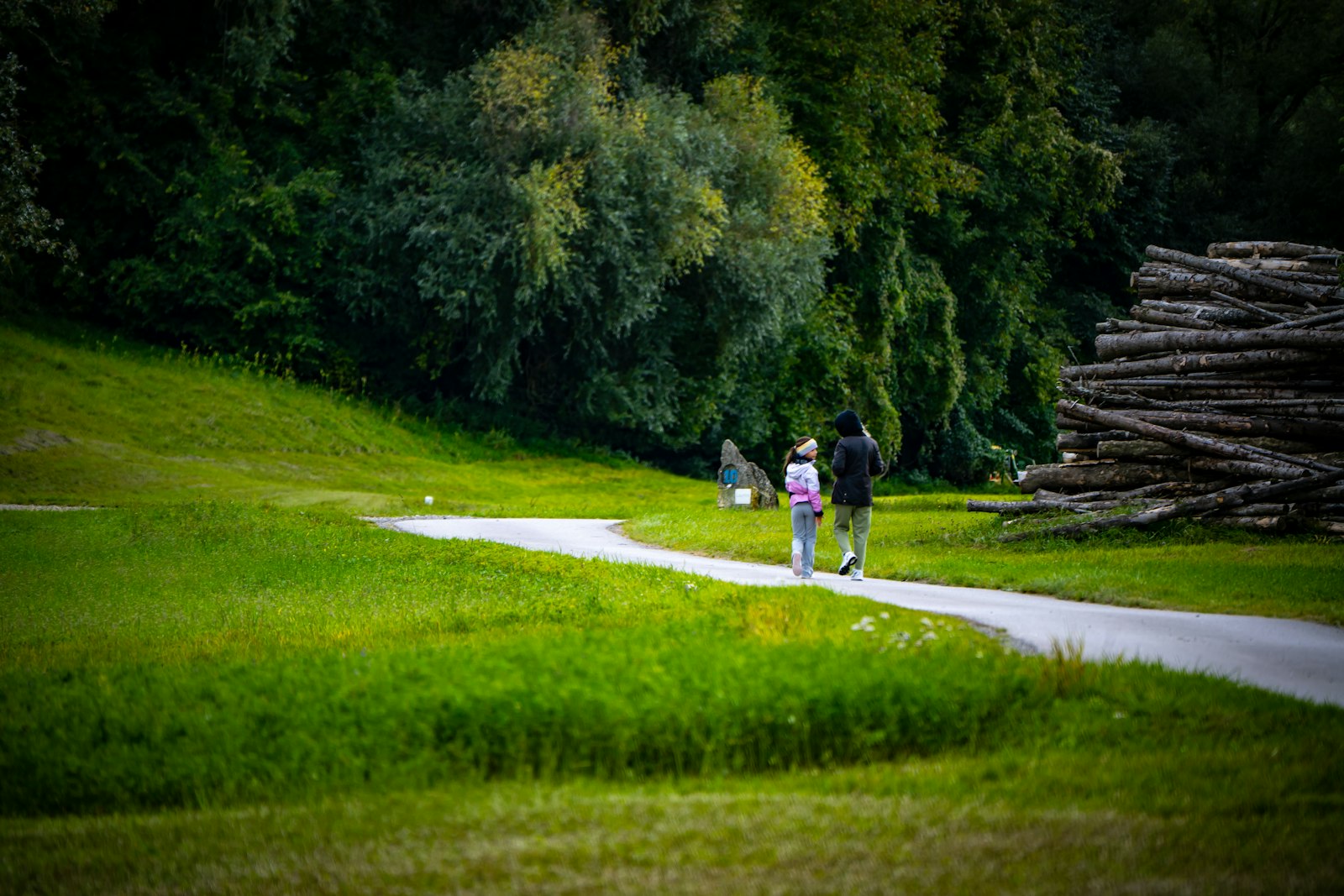 A mother and adult daughter in activewear walking together along a tree-lined path
