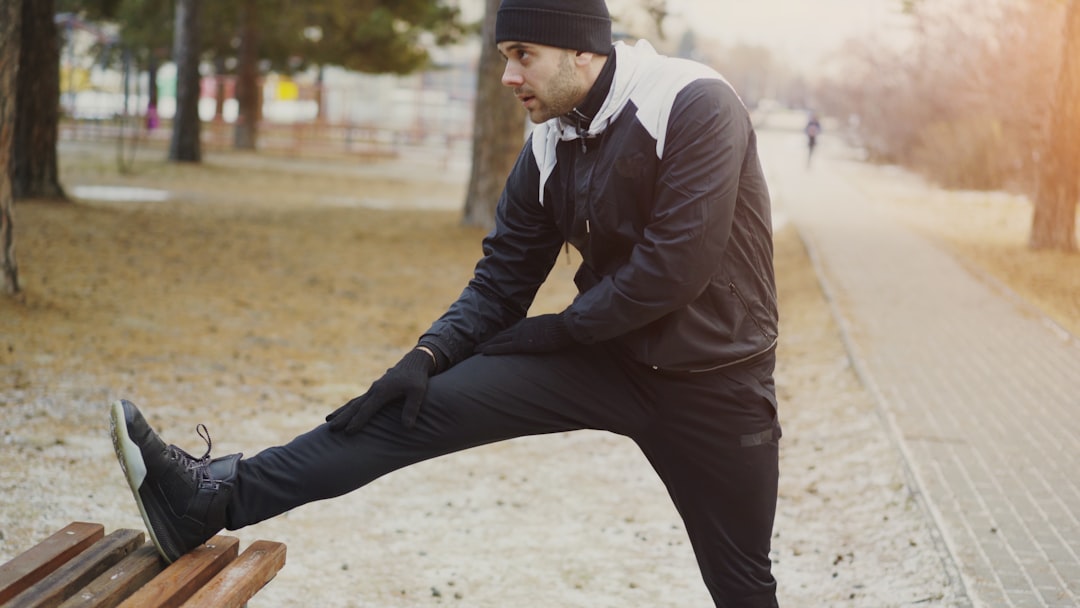 A man stretching his leg on a park bench before a walk in cold weather
