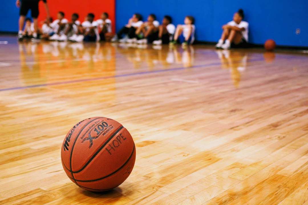 A basketball rests on an indoor court with young players seated behind it