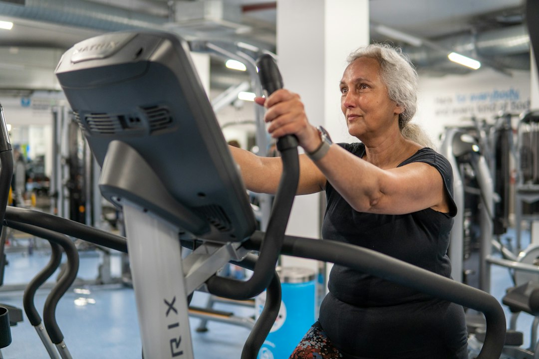 A grey-haired woman exercising on a cross-trainer in a gym