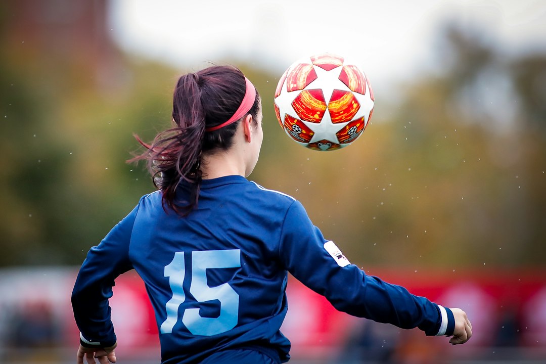 A young female football player in a blue jersey controls the ball during a match