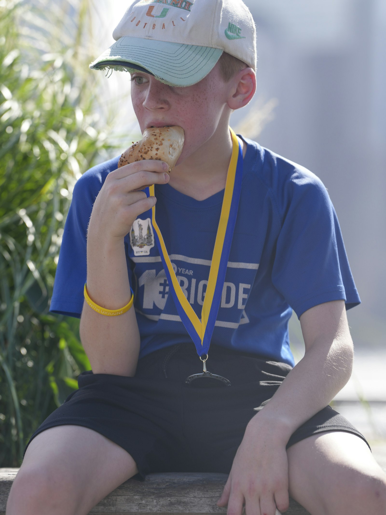 A young boy wearing a finish-line medal eats a bagel after a kids fun run