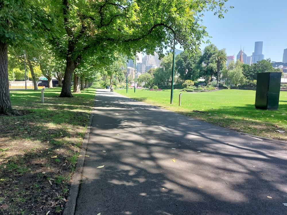 A sealed path through Alexandra Gardens with trees, lawns and Melbourne's skyline in the background