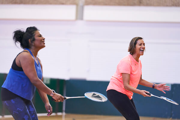 Two woman people playing badminton on a court